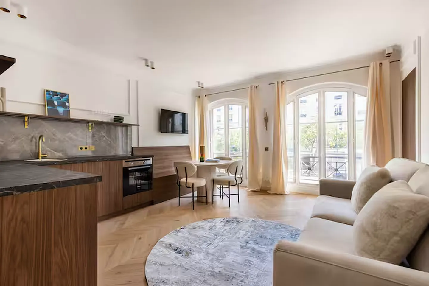 Séjour lumineux avec cuisine ouverte en bois, canapé beige et deux grandes portes-fenêtres